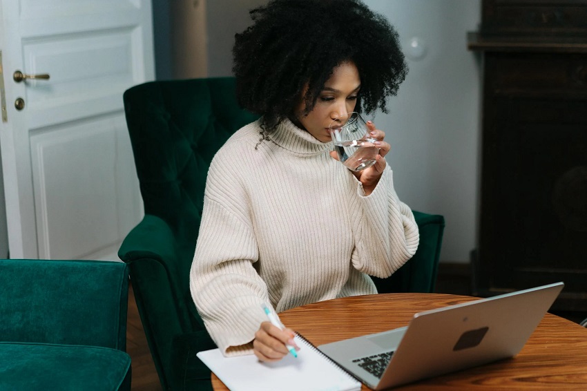 A person sipping water while taking notes and working on a laptop, focusing on 10 graphic design hacks to 10X social media growth.