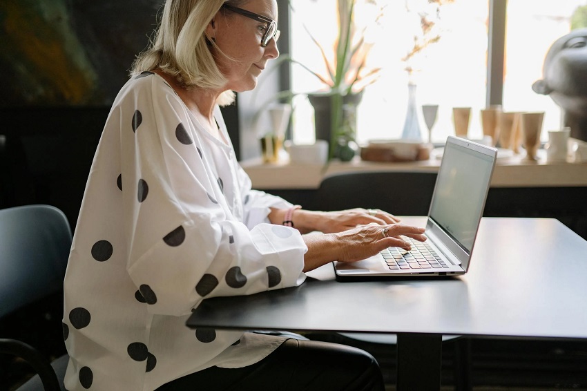A woman in a stylish polka-dot blouse working on a laptop in a modern café, applying 10 graphic design hacks to 10X social media growth.